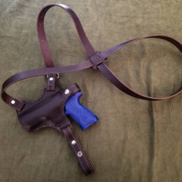 A handmade leather shoulder holster and a gun laying on a bed.