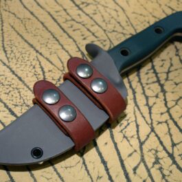 a Scout Style Benchmade Bushcrafter Kydex Sheath with a red leather handle on a table.