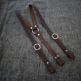 A pair of Handmade Leather Suspenders laying on top of a gray cloth.