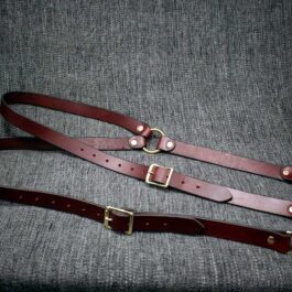 A pair of handmade brown leather suspenders on a gray cloth.