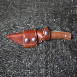 A handmade leather sheath for the Lionsteel M4 sitting on top of a gray cloth.