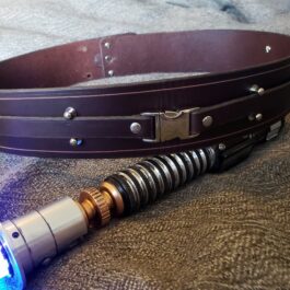 A light saber sitting on top of a bed next to a Handmade Leather Space Wizard Belt.