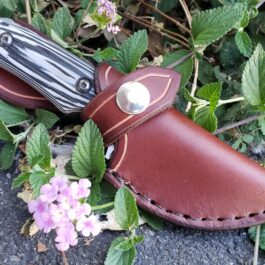 a knife case sitting on the ground next to flowers.