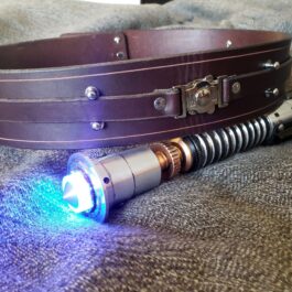 A Handmade Leather Space Wizard Belt with a light on it laying on a bed.