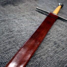 A Handmade leather Scabbard for the Albion Liechtenauer sitting on top of a table.