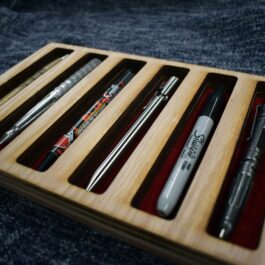 A wooden pen tray with pens and pencils in it.