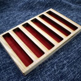 A close up of a Wooden Pen Tray with red strips in it.