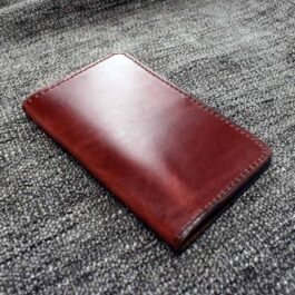 A Field Notes Wallet, made of brown leather, laying on top of a bed.