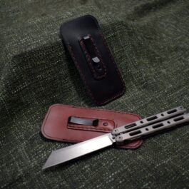 A Benchmade 85/87 Balisong Slip with Pocket Clip and sheath sitting on a green cloth.