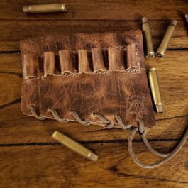 A Handmade Leather Buttstock Cover with eight bullet cases on a wooden table.