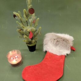 A Handmade Reindeer Fur Christmas Stocking next to a small christmas tree.