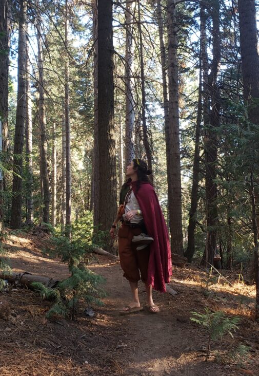 A woman in a Linen Hooded Cloak walking through a forest.