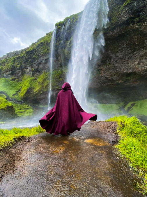 Boiled Wool Hooded Cloak in burgundy worn in front of a waterfall