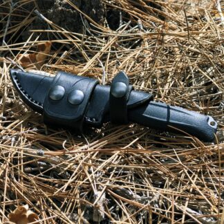 a black knife laying on top of a pile of dry grass.