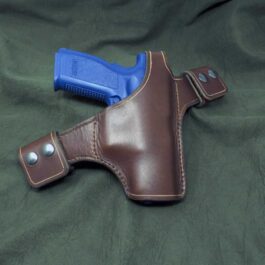 A brown and blue Handmade Leather Snap Loop Pancake Holster laying on a green cloth.