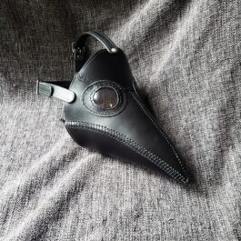 A Handmade Leather Plague Doctor Mask laying on top of a gray cloth.