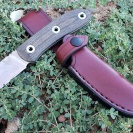 A Leather Sheath for the Benchmade Pardue Hunter that is laying on the ground.
