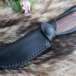 A Vertical Leather Sheath For The Benchmade Saddle Mountain Skinner laying on top of a fur covered ground.