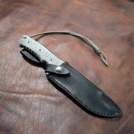 A Chris Reeve Pacific with a Handmade Leather Sheath is lying on a leather surface.