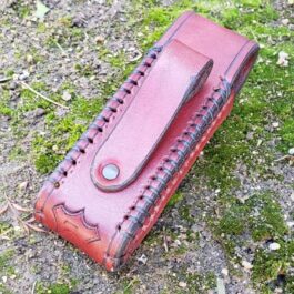 A red Handmade Leather Pouch sitting on top of a grass covered field.