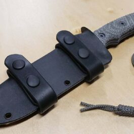 A Kydex Sheath for the Chris Reeve Pacific is laying on a table with a cord.