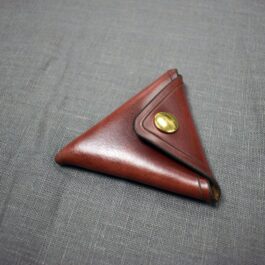 A handmade leather coin pouch sitting on top of a gray cloth.
