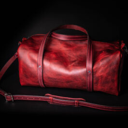 A red Bison Leather Duffel Bag on a black background.