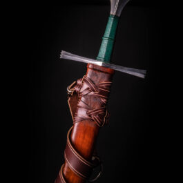 A hand holding a knife with a green blade in a Custom Wood Core Scabbard.