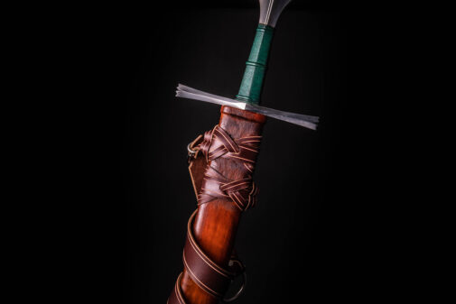 A hand holding a knife with a green blade in a Custom Wood Core Scabbard.