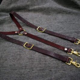 A pair of bison leather suspenders on a gray cloth.