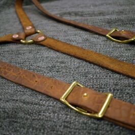 A pair of Bison Leather Suspenders sitting on top of a gray blanket.