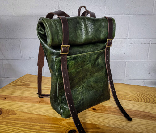 A bison leather roll top rucksack sitting on top of a wooden table.