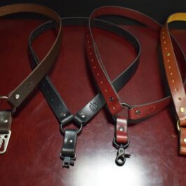Two brown, one red, and one black leather single point sling laid on a wooden table - Grommet's Leathercraft - renaissance clothing - renaissance art clothing - renaissance era clothing - leathercraft supplies - leathercraft accessories - leathercraft store near me - quality leather craft