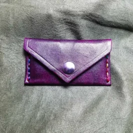 A purple leather Business Card Wallet sitting on top of a bed.