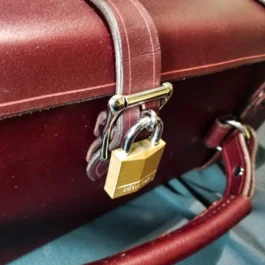 A red Handmade Leather Suitcase with a padlock attached to it.