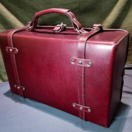 A red Handmade Leather Suitcase sitting on top of a table.