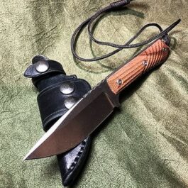 A Leather Scout Sheath for the Chris Reeve Nyala laying on top of a green cloth.