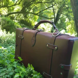 A handmade leather suitcase sitting in the middle of a lush green forest.