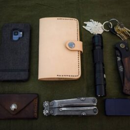 A Leather Field Notes Cover, keys, knife, wallet, and other items laid out on a.