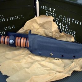 A Ka Bar Fighting Knife with its Kydex sheath laying on top of a piece of paper.