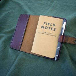 A leather field notes cover laying on a green sheet.