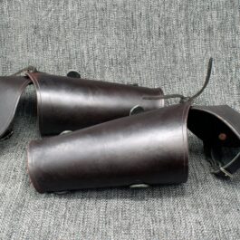 A pair of Brown Leather Vambraces with Attached Elbow Armor sitting on top of a couch.