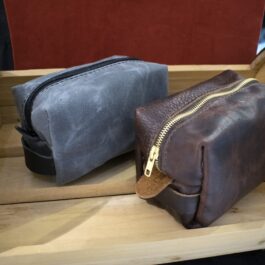 A couple of Canvas Dopp Kits/ Toiletry Bags sitting on top of a wooden shelf.