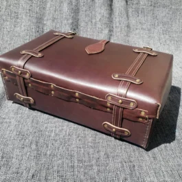 A handmade leather suitcase sitting on top of a gray couch.