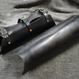 A pair of Handmade Leather Greaves sitting on top of a bed.