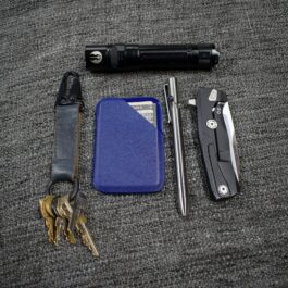 A Kydex wallet, keys, knife, and other items laid out on a carpet.