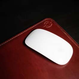 A handmade leather mouse pad sitting on top of a red leather case.