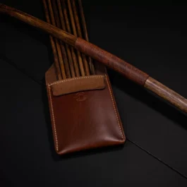 A brown Leather Pocket Quiver sitting next to a wooden stick.