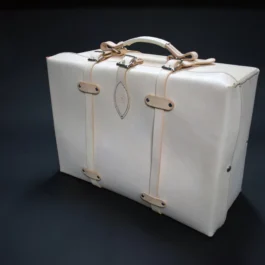 A white Handmade Leather Suitcase sitting on top of a black floor.