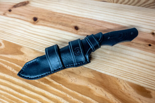 A Benchmade Fixed Contego knife with a black Leather Sheath for the Benchmade Fixed Contego on a wooden table.